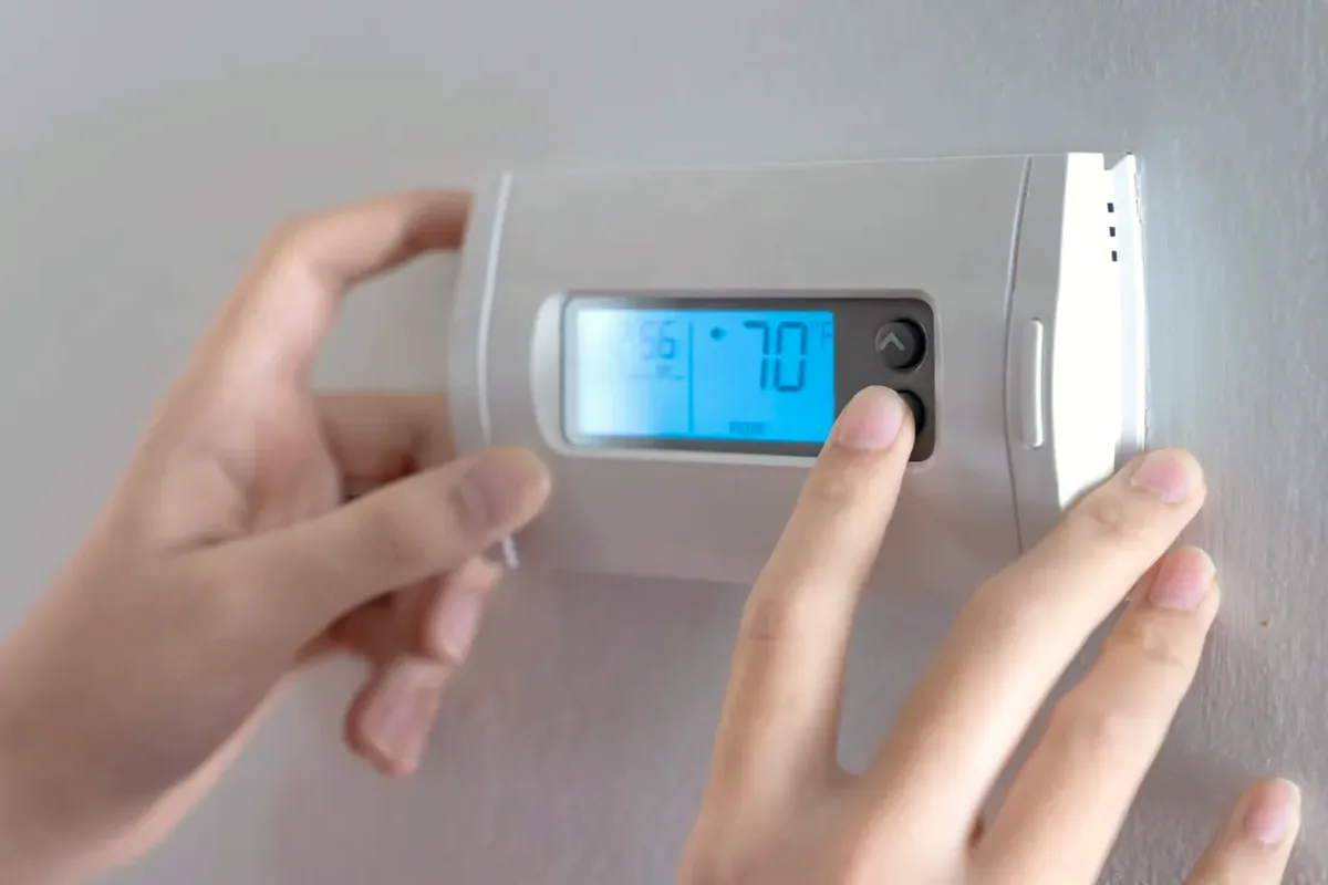 Hands adjusting a digital wall thermostat